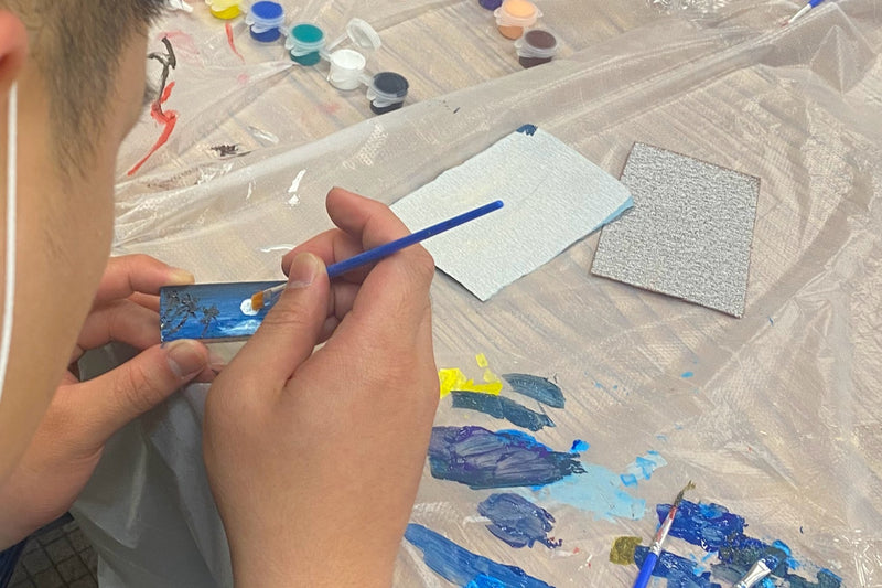 創作過程：特寫手部細心繪製木製鑰匙圈上的月亮與樹