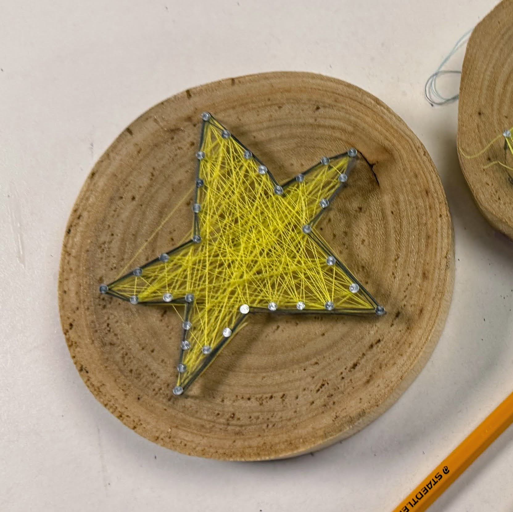 成品：圓木片線畫手工藝品，以黃色線纏繞成五角星圖案