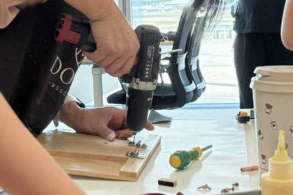 創作過程：學員使用電鑽在木製平板支架上鎖螺絲組裝