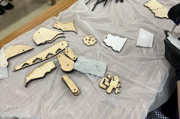 創作過程：雷射切割的長頸鹿檯燈木製零件散佈在桌面上，準備組裝