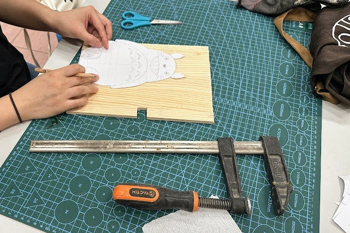 創作過程：學員將龍貓圖案紙樣貼在木板上，準備製作造型時鐘